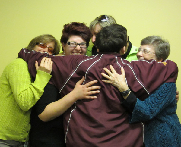 One of the older students has his arms around all four instructors, who are laughing and hugging the student.